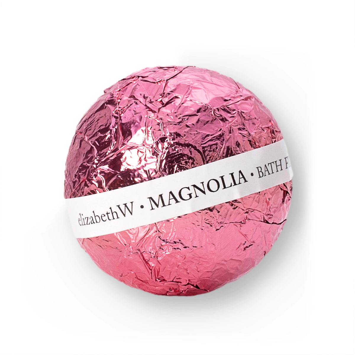 A pink bath fizzy ball wrapped in crinkled foil. There is a white paper band around it with text that reads "E WIGHTMAN &amp; CO • MAGNOLIA BATH FIZZ BALL.” The foil reflects light, giving it a glossy appearance. Drop this fragrant fizz into your bath and let the soothing aromas enchant you.