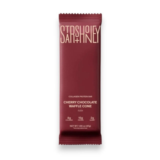 A maroon protein bar wrapper labeled “STARS+HONEY” displays the flavor “CHERRY CHOCOLATE WAFFLE CONE” with nutrition highlights: 8g collagen, 15g protein, and 2g sugar, all set against a beige background. This indulgent treat puts the rich chocolate and tart cherry combination front and center.
