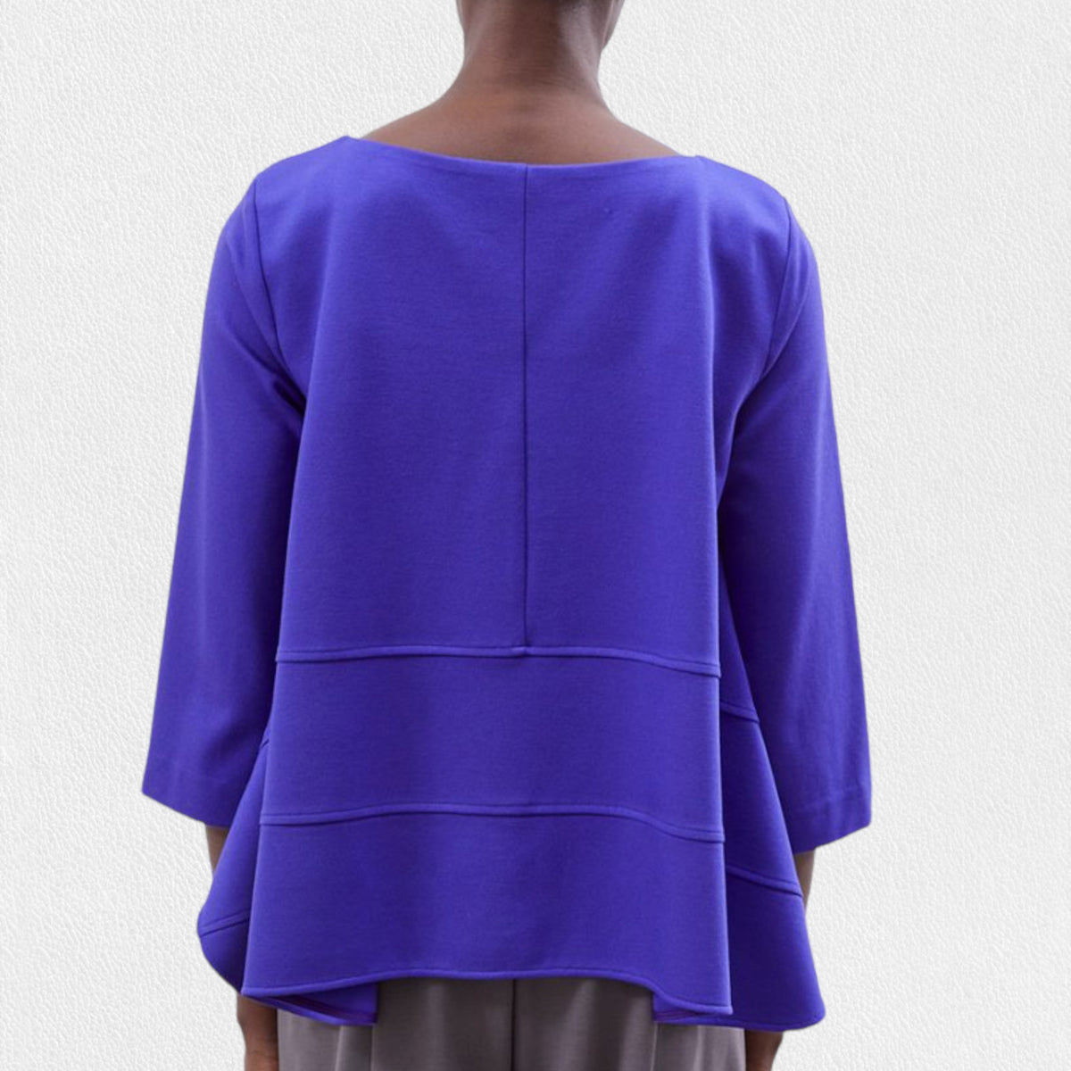 A person is wearing the MEIMEIJ - OVERSIZED CREW NECK TOP by MEIMEIJ, featuring a loose-fitting, long-sleeve design in royal blue with horizontal seam details across the front. Made in Italy, this top has a round neckline and slightly flares out at the bottom. Only the upper torso is visible against a plain, off-white background.