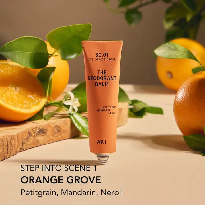 An orange tube and box of AKT LONDON’s DEODORANT BALM ORANGE GROVE—an eco-friendly, aluminum-free deodorant with petitgrain, mandarin, and neroli—are shown on a beige surface against a soft cream background.