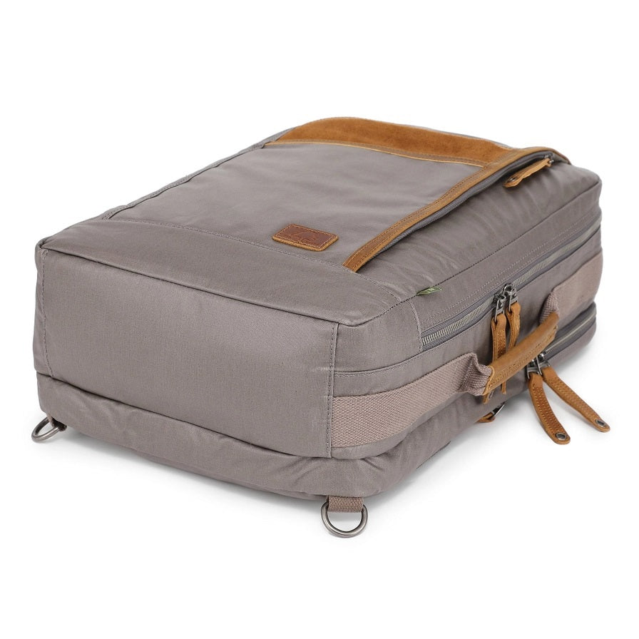 A close-up of the TSD BRAND - MADRONE Coated Canvas Backpack in Grey shows its brown leather accents and an unzipped front pocket with a black wallet partially visible inside.