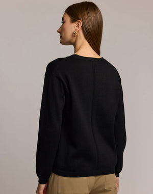 A woman with straight brown hair wears the HINSON WU CASSIE Long Sleeve Cotton Silk Cardigan in camel, styled with black pants. She poses confidently, one hand to her chin, against a neutral backdrop.