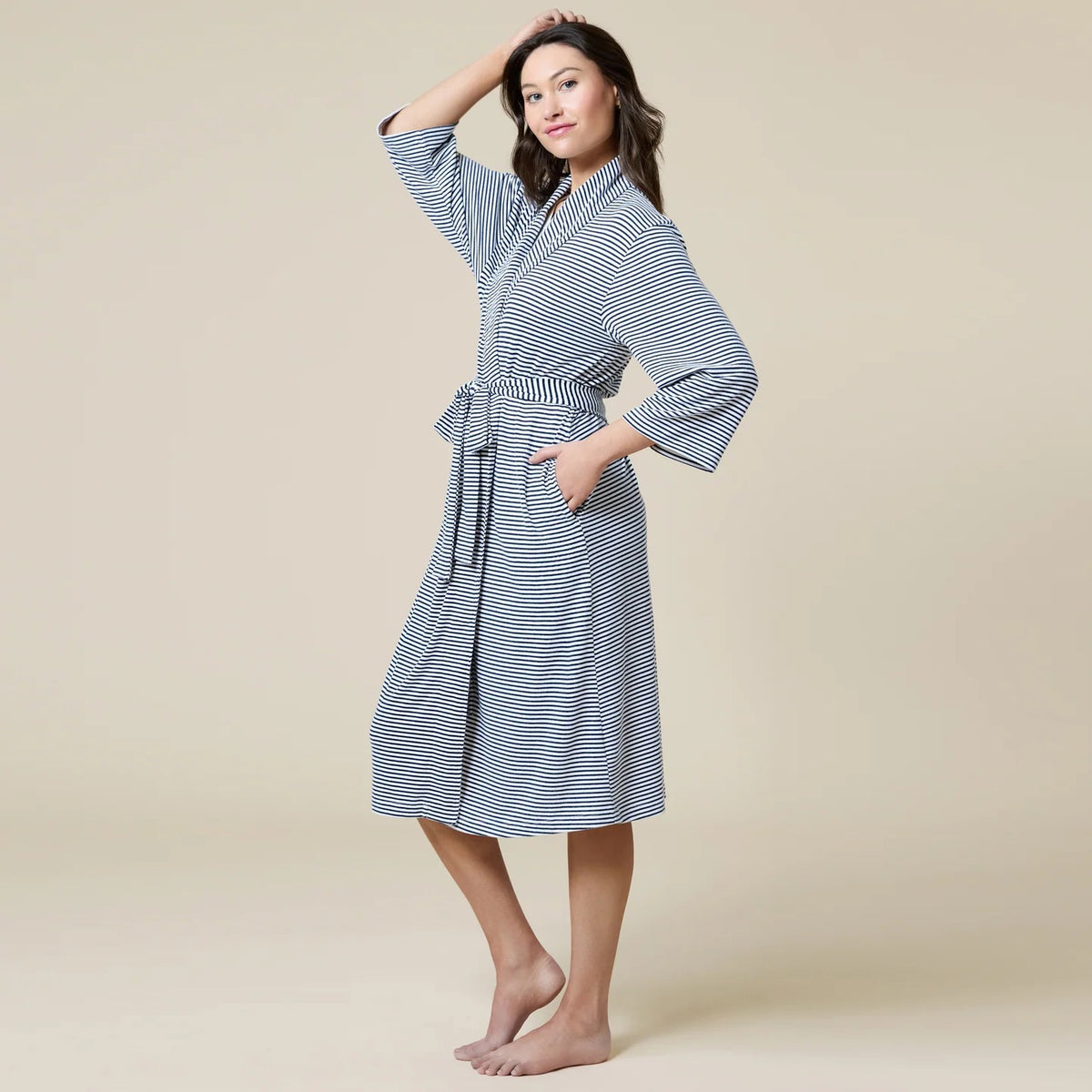 A woman wears a SOFTIES - DREAM SHAWL COLLAR ROBE in pink and white stripes, featuring a shawl collar, a tie waist, and three-quarter length sleeves.