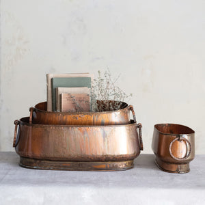 The CREATIVE COOP OVAL METAL PLANTER WITH RING HANDLES, MEDIUM, features an antique copper finish with natural patina—ideal for farmhouse decor and displayed against a white background.