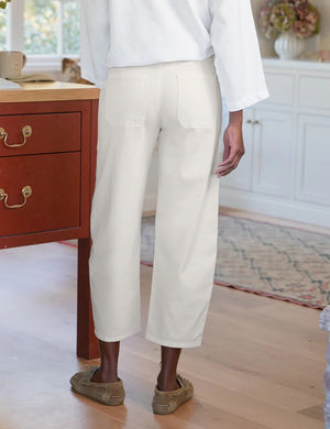 A person wearing FRANK & EILEEN’s Bray Everyday Barrel Pant in Italian Peached Twill Chalk pairs them with a white long-sleeve top, standing casually with one hand in their pocket.