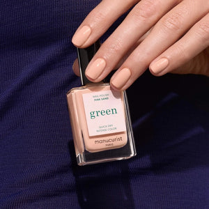 A bottle of MANUCURIST - GREEN™ NAIL POLISH IN PINK SAND by MANUCURIST INC, presented in a rectangular glass bottle with a black cap and a label displaying “green,” along with the phrases “quick dry” and “intense color.”.