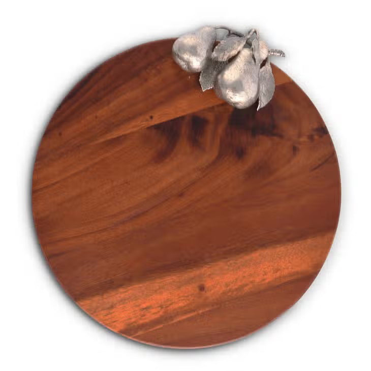 The PEAR CHEESE TRAY by VAGABOND HOUSE is a round wooden board with a smooth, polished surface, showcasing richly colored wood. It features a natural, reddish-brown grain pattern and is adorned with a pure-pewter silver pear-shaped handle detailed with leaves at the top right corner. The background is white.