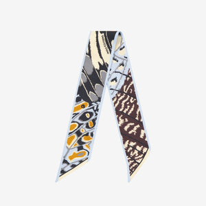 The INOUI EDITIONS - PAPILLON (BUTTERFLIES) SILK RIBBON by INOUI features a butterfly wing print in orange, black, white, and yellow—an elegant silk scarf to elevate any outfit. Displayed on a white background.