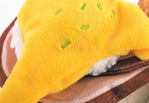 Introducing the PLAY PET LIFESTYLES/BRANDS BARKING BRUNCH - BENNY’S BENEDICT: an adorable dog toy designed to look like a plush egg with a yellow yolk atop a round, brown base, mimicking a classic brunch favorite. Perfect for playful pups, this fun and charming brunch-themed toy features a black fabric tag attached at the bottom.