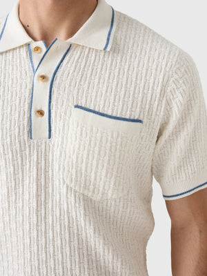 A smiling gray-haired man in sunglasses and khaki pants wears the CRIQUET Bungalow Sweater Polo in White, featuring a blue-trimmed collar and pocket, standing against a plain background.