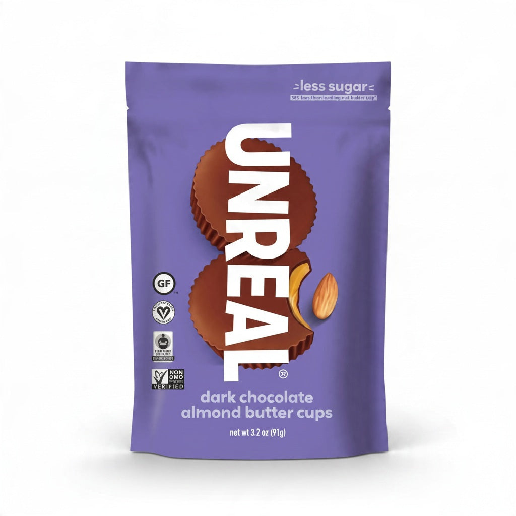 A purple package of UNREAL - DARK CHOCOLATE ALMOND BUTTER CUPS featuring vegan, gluten-free, and non-GMO icons, with one cup bitten to show the interior.