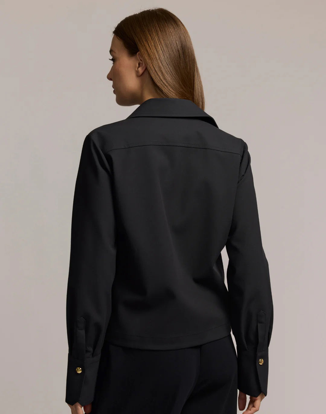 A woman with long brown hair models the HINSON WU - ASTRID LONG SLEEVE TRAVELER&#39;S TWILL SHIRT JACKET in dark green over an olive top and blue jeans, showcasing versatile HINSON WU travel style with gold hoop earrings against a neutral background.