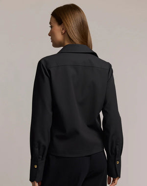 A woman with long brown hair models the HINSON WU - ASTRID LONG SLEEVE TRAVELER'S TWILL SHIRT JACKET in dark green over an olive top and blue jeans, showcasing versatile HINSON WU travel style with gold hoop earrings against a neutral background.