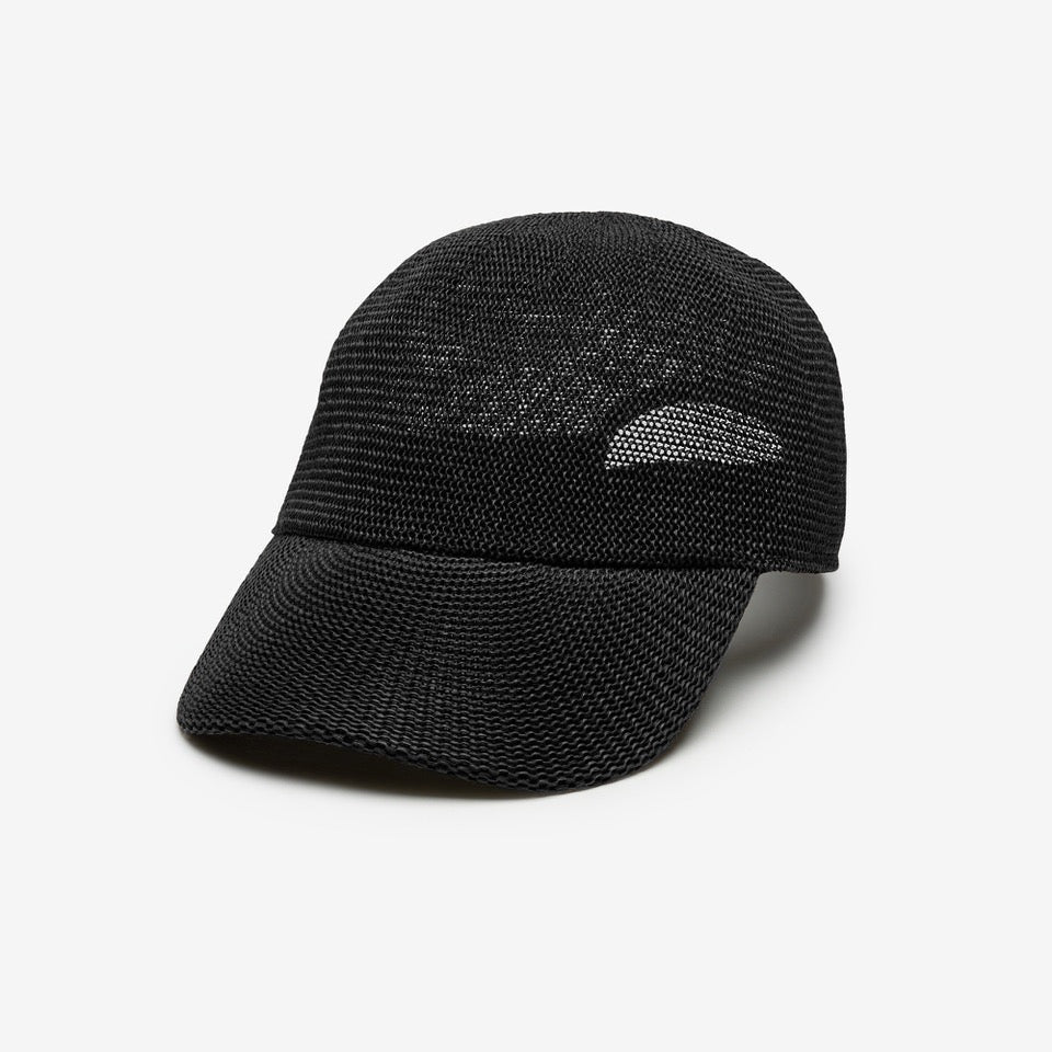 A woman with long brown hair wears the WYETH HATS - PAULA MESH CAP IN BLACK by WYETH and a brown and navy checkered shirt, standing against a plain white background.
