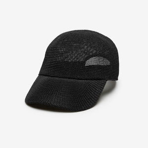 A woman with long brown hair wears the WYETH HATS - PAULA MESH CAP IN BLACK by WYETH and a brown and navy checkered shirt, standing against a plain white background.
