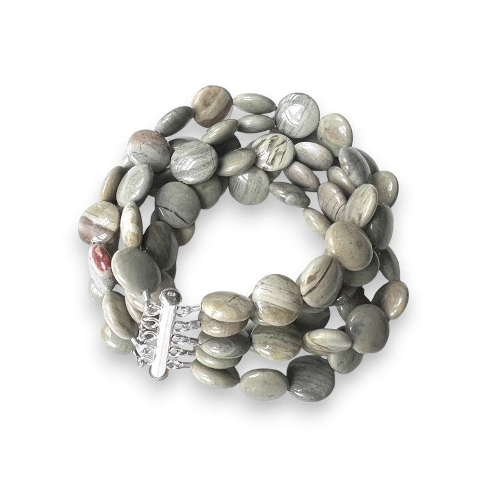 The ANN LIGHTFOOT - SILVER LACE AGATE DISC CUFF by ANN LIGHTFOOT is a multi-strand beaded cuff bracelet featuring smooth, round, greenish-grey stones and a shiny silver slide clasp that secures the strands. Some beads, made of silver lace agate, showcase subtle natural patterns and color variations.