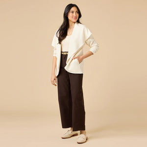 A woman wears an off-white SOFTIES - DREAMTECH EXAGGERATED COLLAR CARDIGAN with an exaggerated waterfall collar, cinched at the waist with a thin belt, and holds a matching handbag.