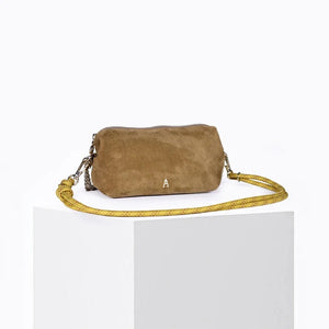 The CRAIE STUDIO - NUAGE SUEDE SEPIA MINI BAG, a compact brown suede shoulder bag featuring a zipper and a long yellow strap, is showcased on a white pedestal against a light background.