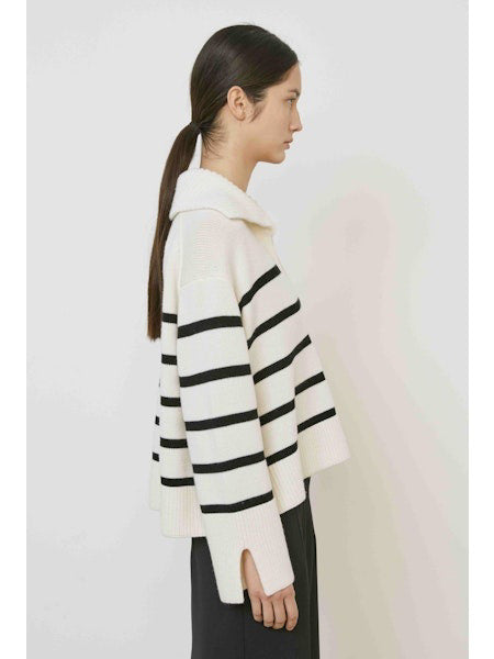 A woman with straight dark hair models the MEIMEIJ STRIPE SWEATER—a cream sweater with black horizontal stripes and a large collar—paired with a plain black skirt, standing against a white background.