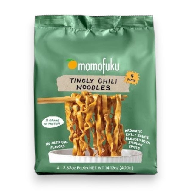 A bag of MOMOFUKU - TINGLY CHILI WAVY NOODLES is displayed with three additional packs in the background. An inset shows a spiciness scale with four out of five peppers highlighted. The packaging showcases air-dried wavy noodles on chopsticks alongside product details, emphasizing their Sichuan-inspired flavor from MOMOFUKU.