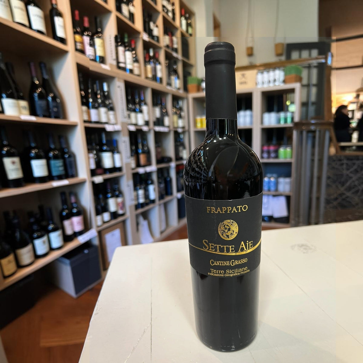 A bottle of CANTINE GRASSO FRAPPATO 2025 red wine with a black label, standing on a white surface in front of wine store shelves.