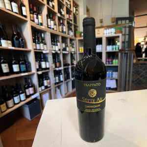 A bottle of CANTINE GRASSO FRAPPATO 2025 red wine with a black label, standing on a white surface in front of wine store shelves.