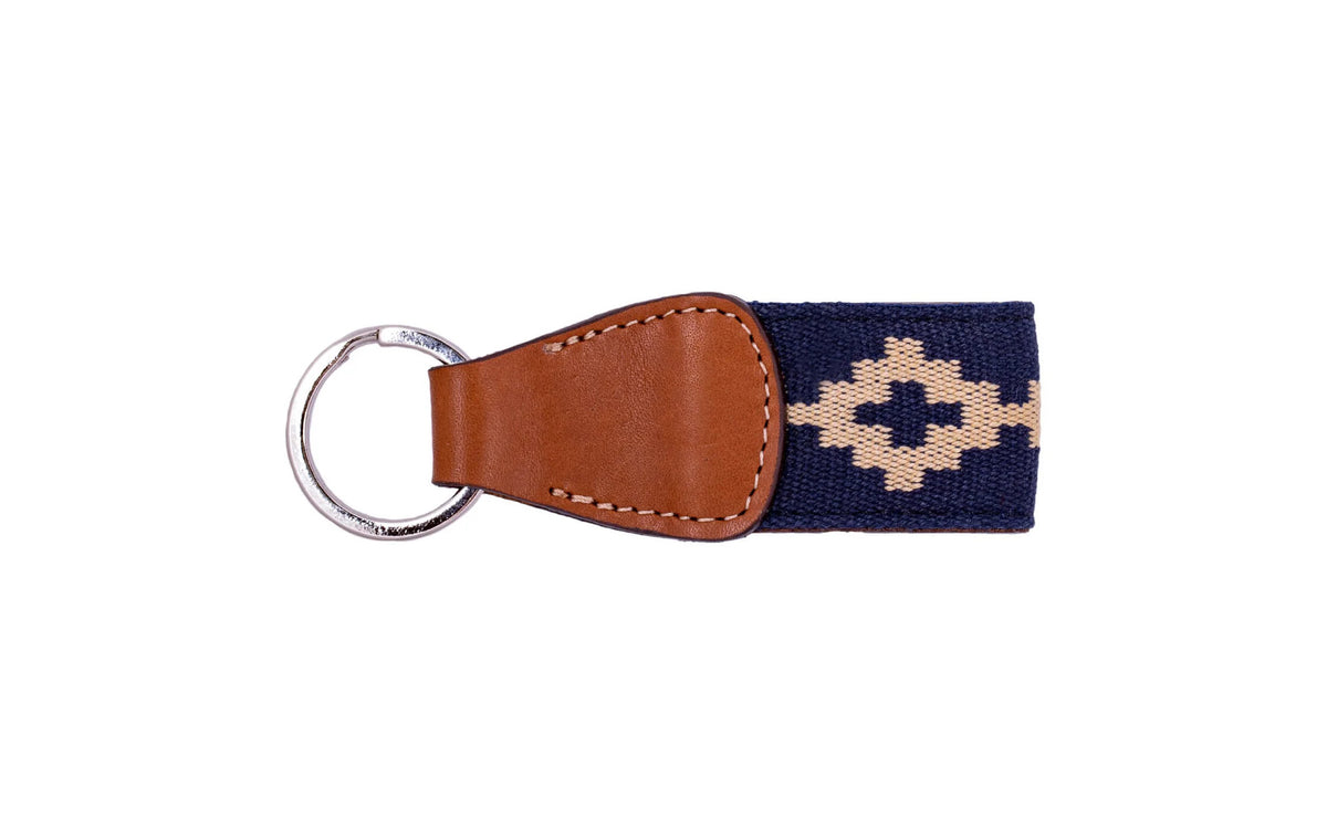 The LA MATERA - CORBINA WOVEN KEYCHAIN by LA MATERA features a silver metal ring, brown leather, and a navy blue strap with a beige diamond pattern inspired by Argentine artisan designs.