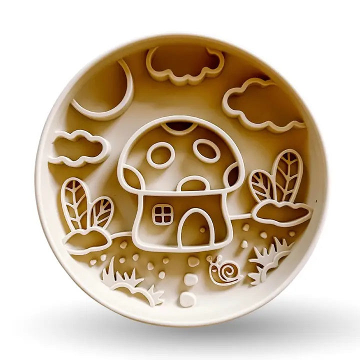 Introducing the MUSHROOM SLOW FEEDER by BARKS & BROWNIES—a round beige plate featuring raised sections that create a delightful scene of a mushroom house, clouds, moon, plants, grass, and a small snail in the foreground. Thoughtfully outlined to keep food separated, this charming design encourages slower eating for your pup while making mealtime more enjoyable.