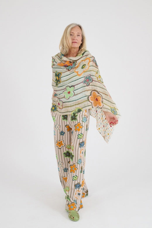 A woman with shoulder-length blonde hair wears a light blue T-shirt, a beige STORIATIPIC - ANNE SCARF, and a beige skirt with embroidered flowers, standing against a plain white background.