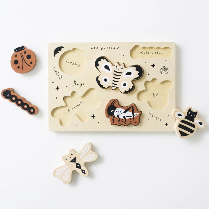 The BUGS TRAY PUZZLE by WEE GALLERY is a wooden puzzle set on a light background, showcasing six insect pieces: a ladybug, a caterpillar, a moth, a bee, a cricket, and a dragonfly. This educational fun bugs set also includes small black stars and the word "Bugs!" emblazoned on the puzzle board.