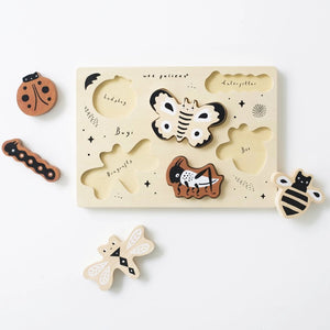 The BUGS TRAY PUZZLE by WEE GALLERY is a wooden puzzle set on a light background, showcasing six insect pieces: a ladybug, a caterpillar, a moth, a bee, a cricket, and a dragonfly. This educational fun bugs set also includes small black stars and the word "Bugs!" emblazoned on the puzzle board.