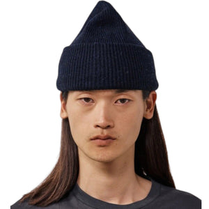 The HARTFORD - SEAMLESS WOOL BEANIE IN NAVY by HARTFORD is a dark blue ribbed knit beanie made from 100% wool, featuring a folded brim and shown against a plain light gray background.