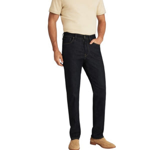 A person wearing 34 HERITAGE - CHARISMA RELAXED STRAIGHT JEANS IN RINSE VINTAGE, a dark blue, vintage-inspired denim by 34 HERITAGE, paired with a beige shirt and shown from the back. The jeans feature brown stitching and a brown leather patch on the waistband.