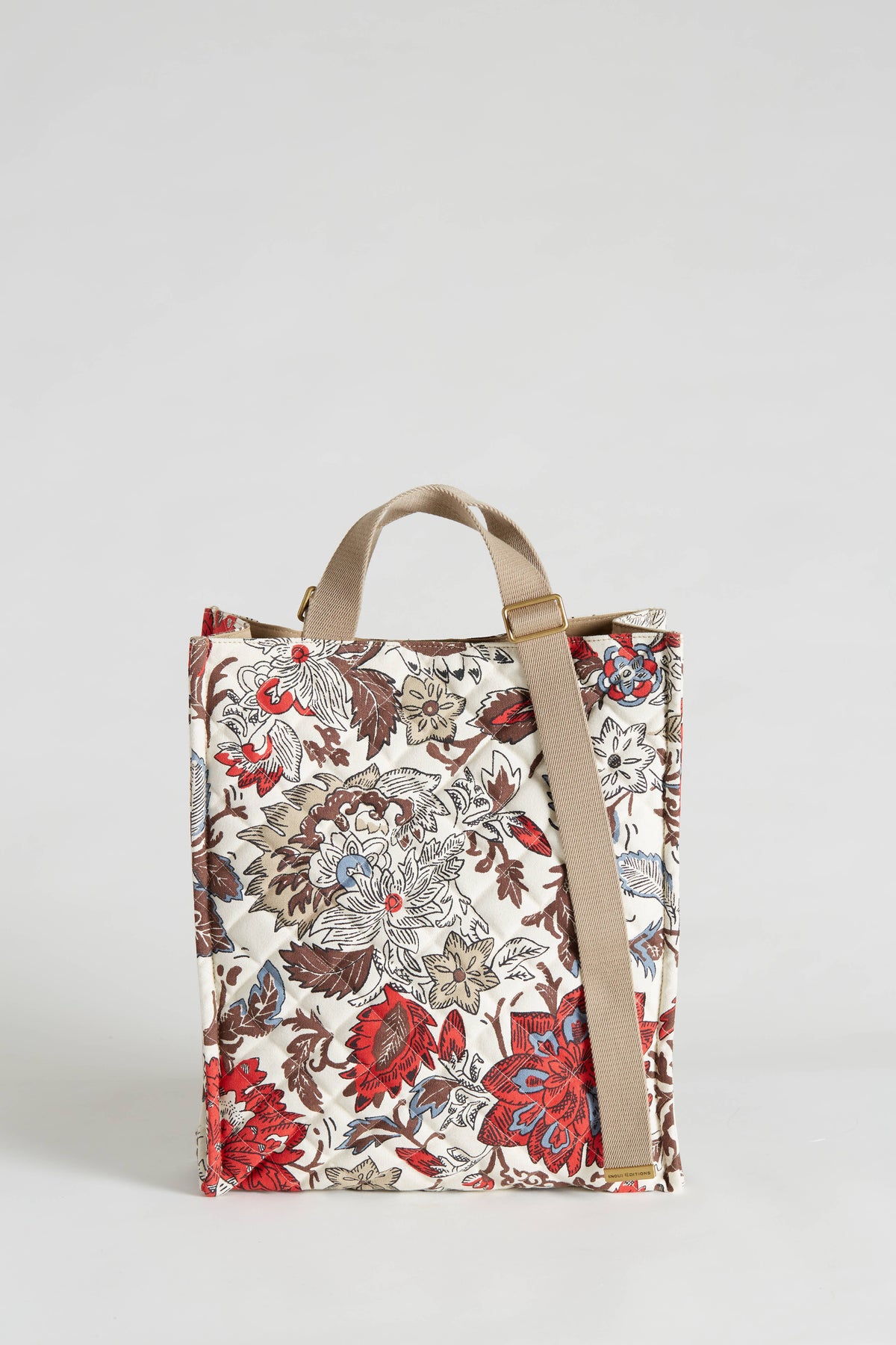 The INOUI EDITIONS - PIPPA STREET BAG by INOUI, a rectangular 100% cotton quilted crossbody tote with beige handles and a strap, is displayed against a plain background. The 40x34x12 cm bag showcases a colorful floral pattern featuring red, blue, and brown flowers on a light background.