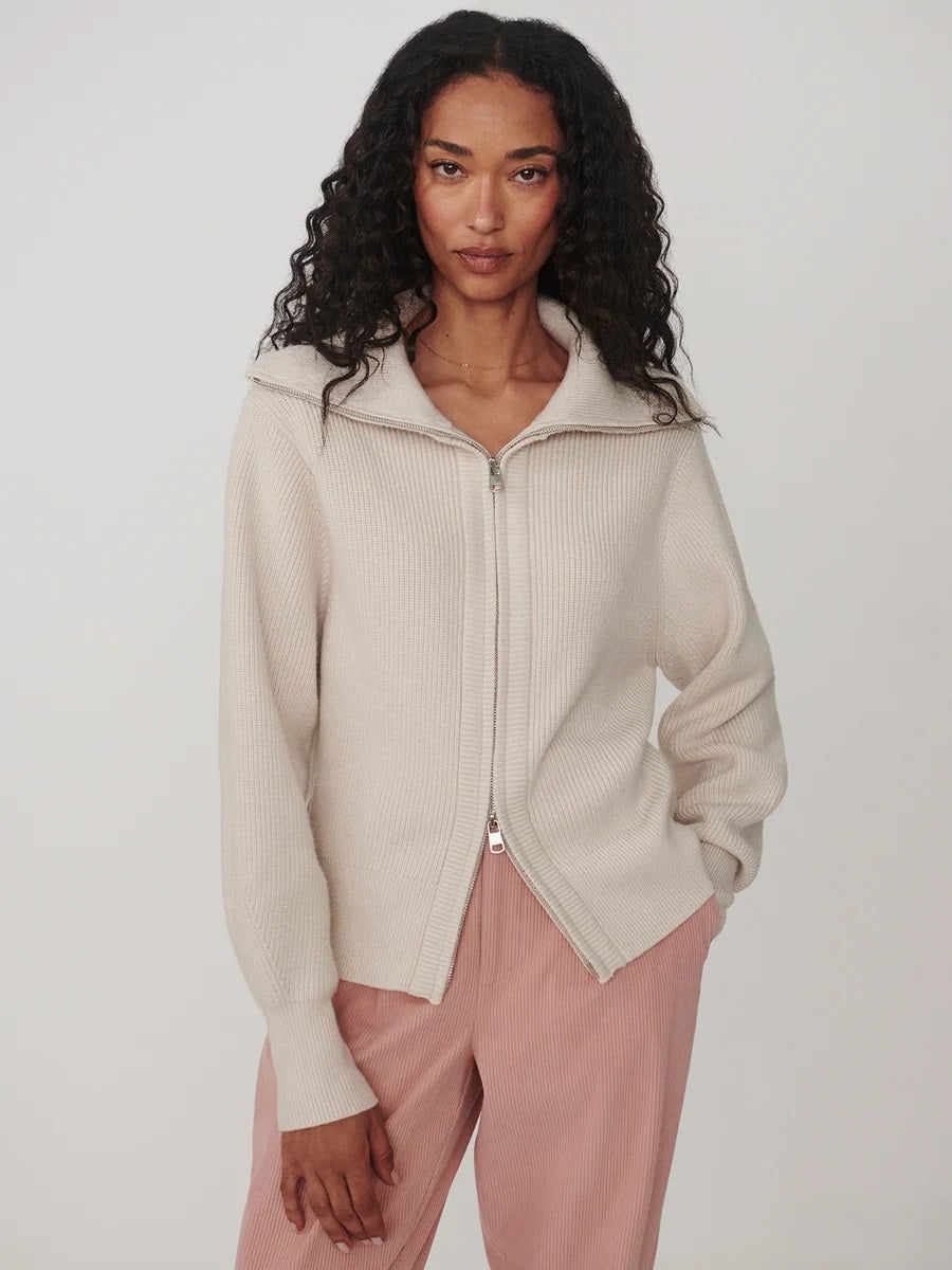 A person wearing a dark brown VARLEY - ENRICO ZIP-THROUGH KNIT JACKET featuring a ribbed soft viscose knit, a high collar, and a front zipper, ideal for cool weather layering.