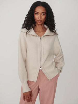 A person wearing a dark brown VARLEY - ENRICO ZIP-THROUGH KNIT JACKET featuring a ribbed soft viscose knit, a high collar, and a front zipper, ideal for cool weather layering.