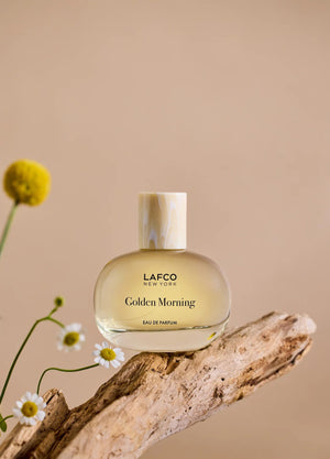 A transparent perfume bottle labeled “LAFCO - FINE FRAGRANCE, GOLDEN MORNING 50ML” by LAFCO features a round, marble-textured cream cap and is displayed against a plain white background. This floral scent is crafted as a vegan and cruelty-free fine fragrance, designed to deliver a sophisticated and conscious olfactory experience.