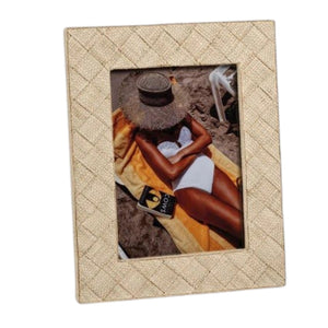 Two beige LA BOCCA WOVEN RAFFIA FRAMES by ZODAX rest on a gray surface. One 5x7 natural raffia photo frame holds an image of a person relaxing by the beach, while the other displays someone wrapped in an orange scarf. Both images are partially obscured, lending a subtle and organic touch to your home decor.
