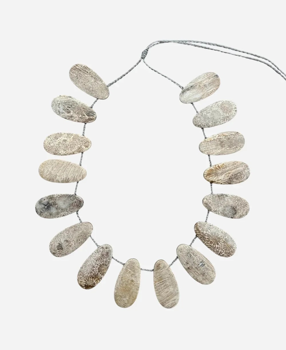 The ANN LIGHTFOOT FOSSIL CORAL FAN NECKLACE features oval, textured white and beige shell pieces on an adjustable cord, arranged in a semicircle against a plain white backdrop.