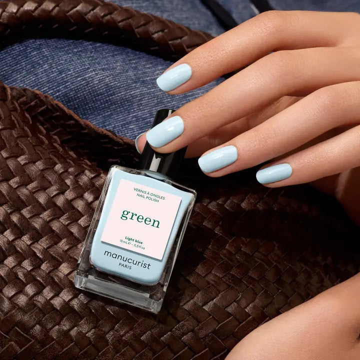 A bottle of MANUCURIST - GREEN™ NAIL POLISH IN LIGHT BLUE by MANUCURIST INC features a sky blue shade and a black cap. The label states: “green, quick dry, intense color.” This bio-sourced nail polish provides a non-toxic formula for vibrant, easy manicures.