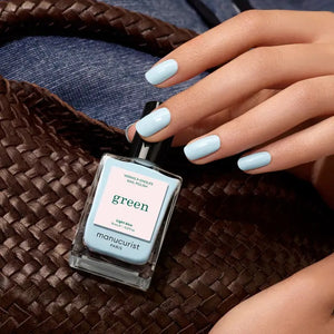 A bottle of MANUCURIST - GREEN™ NAIL POLISH IN LIGHT BLUE by MANUCURIST INC features a sky blue shade and a black cap. The label states: “green, quick dry, intense color.” This bio-sourced nail polish provides a non-toxic formula for vibrant, easy manicures.