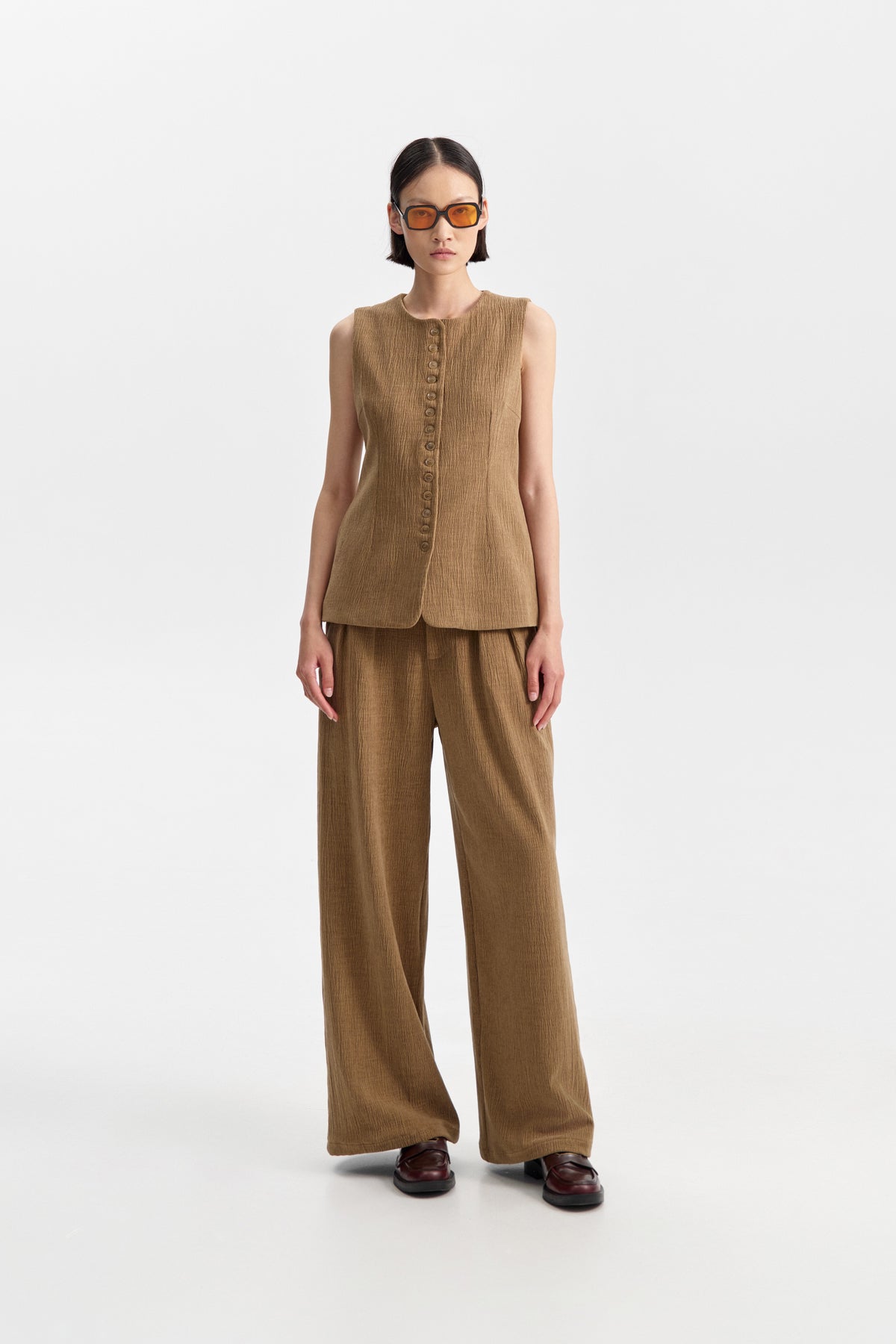ELEH - THE ATLIER VEST by ELEH: A sleeveless, textured brown crinkle fabric vest with a round neckline and small front buttons, shown against a white background.