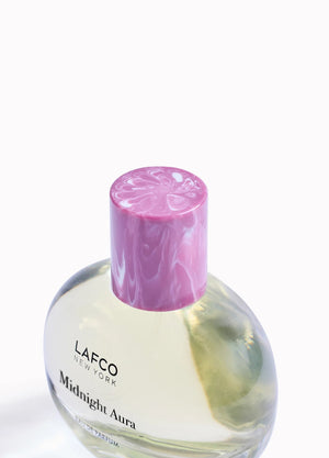 A LAFCO Fine Fragrance, Midnight Aura 50ml box rests on a rock, framed by flowers and green cactus pads in the background, capturing the essence of this alluring fruity perfume crafted with essential oils.