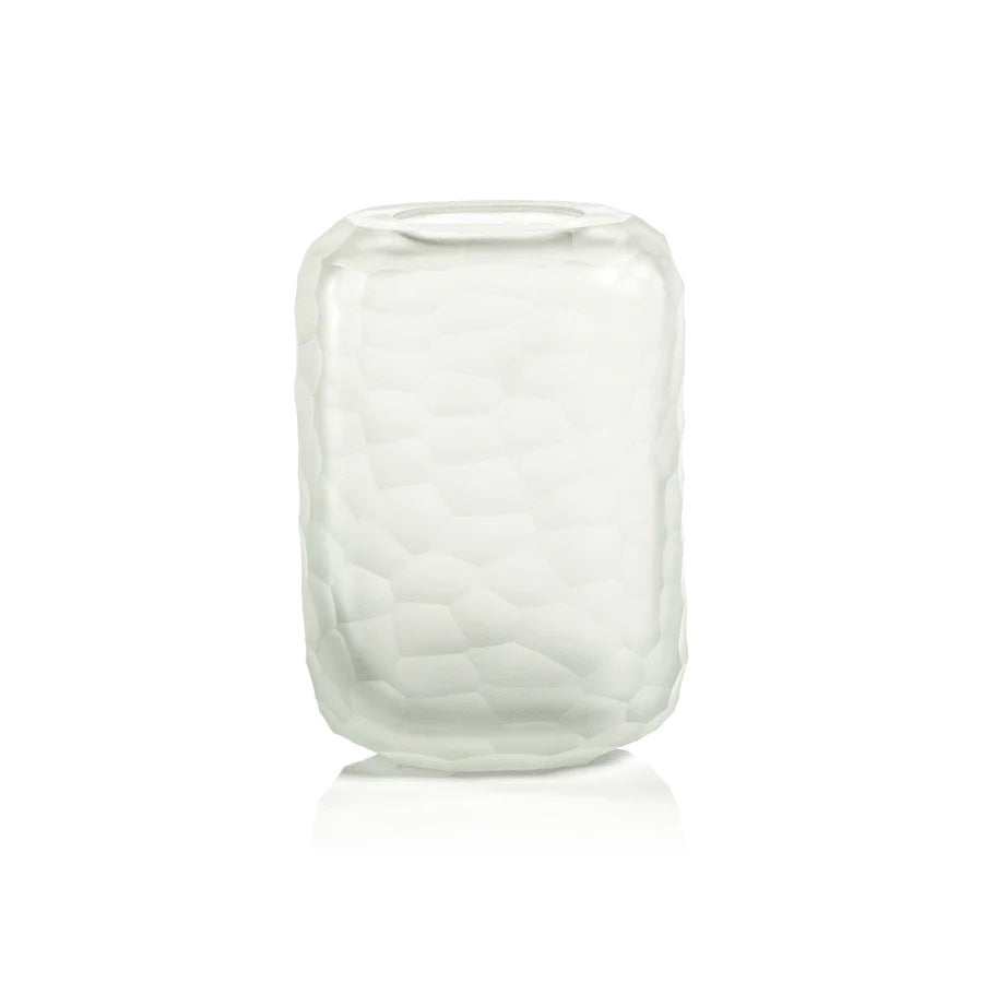 The HAMMERED FROSTED GLASS VASE by ZODAX is a translucent, cylindrical vase featuring a textured hexagonal pattern on its surface. Measuring 12.7 cm x 7.62 cm x 19.05 cm, the vase has a smooth rim and stands upright against a plain white background.