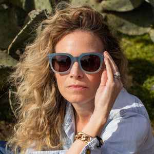 The CADDIS Jockamo Polarized Sunglasses feature a blue-green rectangular design with dark polarized lenses. The premium acetate frame is accented by white-tipped arms, and the brand "Caddis" is prominently displayed on both the lens and arm. These sunglasses combine a vintage aesthetic with a modern, sleek design perfect for casual wear.