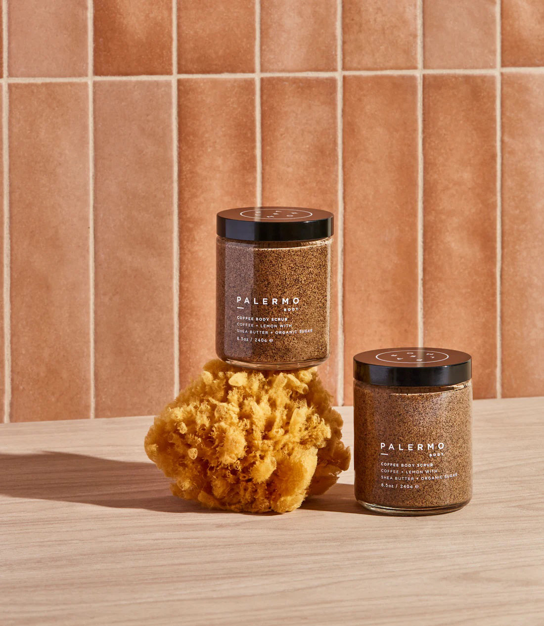 A jar of PALERMO BODY - COFFEE &amp; LEMON BODY SCRUB is shown against a white background. The organic coffee scrub, featuring lemon, shea butter, moisturizing coconut oil, and organic sugar, comes with a black lid. The label details the product information and the quantity is 8.5 oz / 240 g.