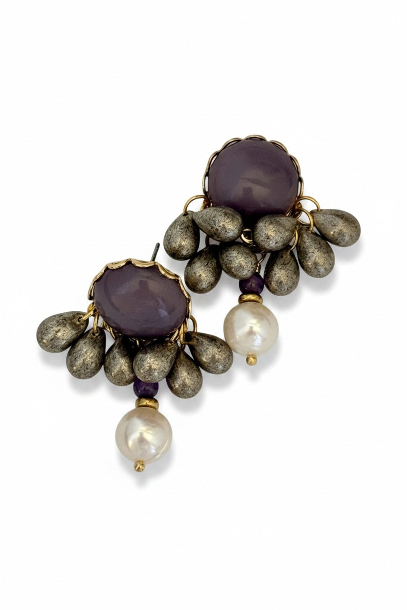 The SANDRINE FRANCE STUDIO - OLWEN EARRINGS by SANDRINE FRANCE STUDIO feature round purple stones encircled by metallic teardrop-shaped beads and finished with a dangling white pearl on each earring, all set against a white background—these handmade earrings from NYC beautifully showcase the perfect balance of elegance and artistry.