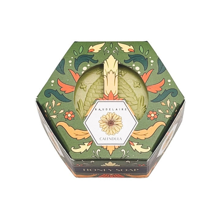 Hexagonal box of BAUDELAIRE - CALENDULA HONEY SOAP 3.5 OZ, featuring green floral packaging with a central clear window displaying the triple-milled moisturizing bar and a floral design label on top, by BAUDELAIRE.