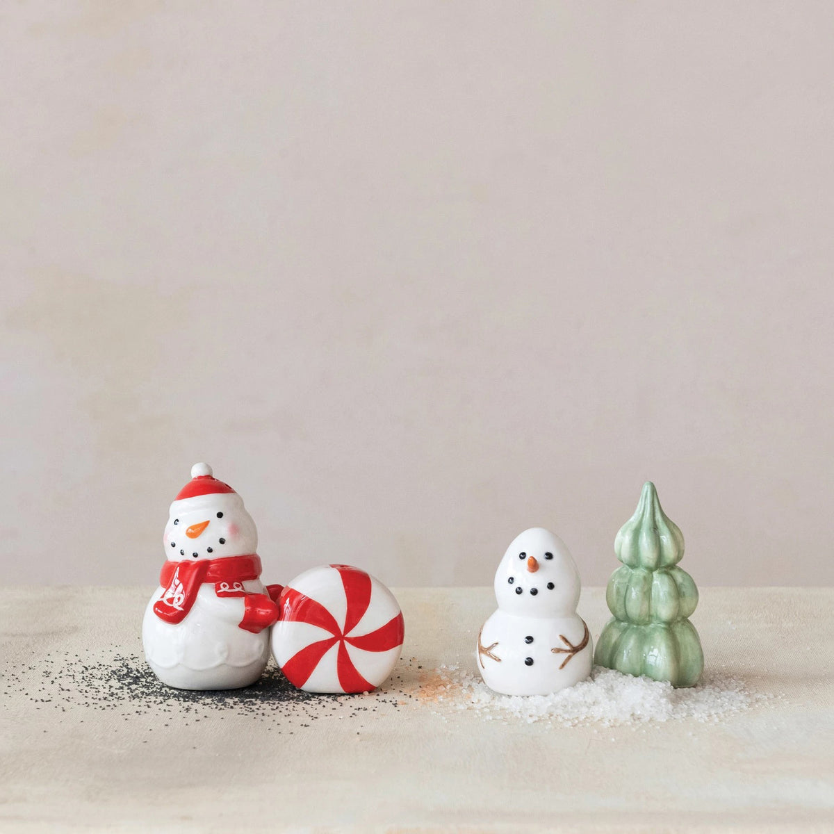 The CREATIVE COOP STONEWARE SNOWMAN AND TREE SALT AND PEPPER SET features a snowman shaker with twig arms and a festive tree-shaped shaker, both displayed on a plain white background.