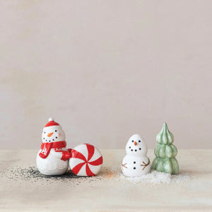 The CREATIVE COOP STONEWARE SNOWMAN AND TREE SALT AND PEPPER SET features a snowman shaker with twig arms and a festive tree-shaped shaker, both displayed on a plain white background.